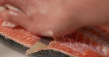 un' qualificato capocuoco affettare e separare colonna vertebrale ossatura su il fresco carne di salmone per Sushi. - vicino su video