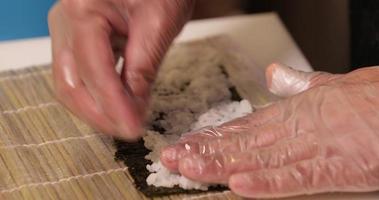 Hands Fast Spreading Sushi Rice On Nori Wrap With Bamboo Mat Underneath - close up video