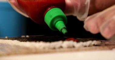 Chef Adding Red Chili Sauce To Seaweed Wrap On Top Of Spread Sushi Rice In Slow Motion - close up, selective focus video