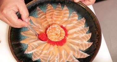 placage de nourriture - chef avec une cuillère à café mettant des caviars rouges autour de la rose de saumon sashimi sur une assiette ronde. - prise de vue en plongée video