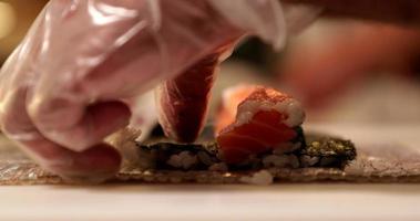 mãos de um chef de sushi rolando rolos de sushi de salmão por uma esteira de bambu na cozinha. fazer rolos de sushi. - tiro de perto video