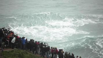 Nazare Portugal - Tourists Watching The Stunning And Famous Big Splashing Waves In Motion - Amazingly Beautiful Attraction - Wide Shot