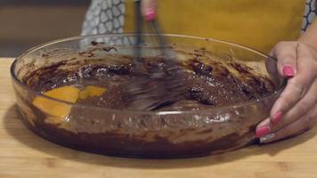 una mujer mezclando huevos en una masa de chocolate guardada en un recipiente transparente - plano medio video