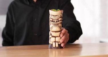 barman servindo coquetel em um tiki de madeira esculpida no balcão do bar do restaurante - fechar video