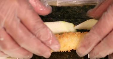 mãos rolando camarão tempura com abacate e pepino em nori usando esteira de bambu em um restaurante de sushi - close-up video