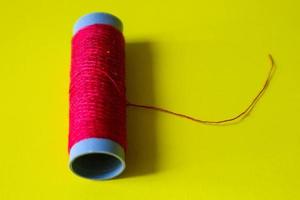 Isolated photo of a roll of red thread above and in front of a yellow background.