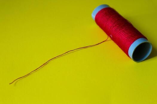 Isolated photo of a roll of red thread above and in front of a yellow background.