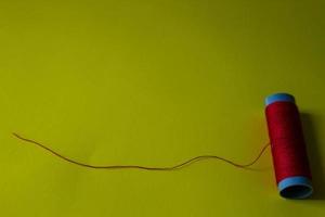 Isolated photo of a roll of red thread above and in front of a yellow background.