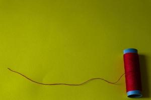 Isolated photo of a roll of red thread above and in front of a yellow background.
