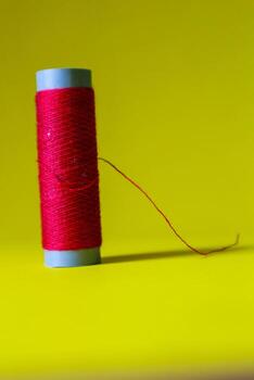 Isolated photo of a roll of red thread above and in front of a yellow background.