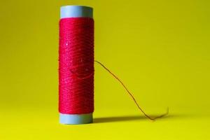 Isolated photo of a roll of red thread above and in front of a yellow background.