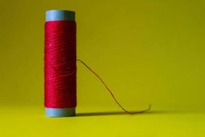 Isolated photo of a roll of red thread above and in front of a yellow background.