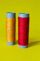 Isolated photo of a roll of red and orange thread above and in front of a yellow background.
