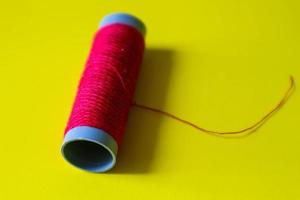 Isolated photo of a roll of red thread above and in front of a yellow background.