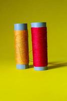 Isolated photo of a roll of red and orange thread above and in front of a yellow background.
