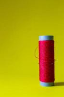 Isolated photo of a roll of red thread above and in front of a yellow background.