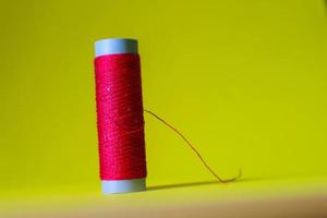 Isolated photo of a roll of red thread above and in front of a yellow background.