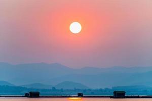 sol sobre montaña y lago al atardecer foto