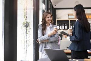 feliz dos jóvenes empresarias asiáticas sosteniendo una taza de café en la oficina de coworking foto