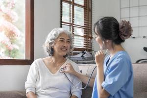 Happy patient is holding caregiver for a hand while spending time together. Elderly woman in nursing home and nurse. photo