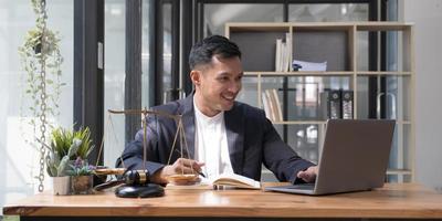 Professional Asian businessman, lawyer or financial consultant in formal suit working at his office desk, using laptop and taking notes on his book photo