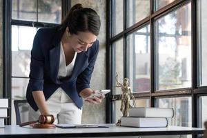 Attractive young lawyer or Businesswoman talking on phone and lawyers discussing contract papers with brass scale on wooden desk in office. Law, legal services, advice, Justice and real estate concept photo