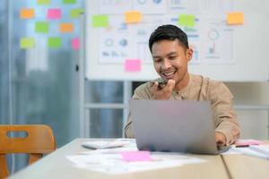 handsome young employee  sitting at desk and looking at computer monitor while answering call in office photo