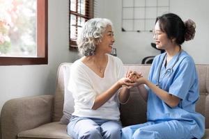 Happy patient is holding caregiver for a hand while spending time together. Elderly woman in nursing home and nurse. photo