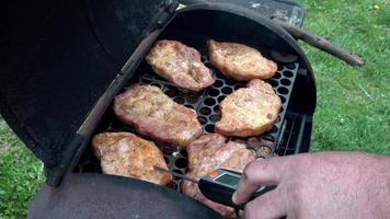Checking for safe food temperature with digital instant thermometer. Kitchen meat thermometer against pork steaks on a grill. video