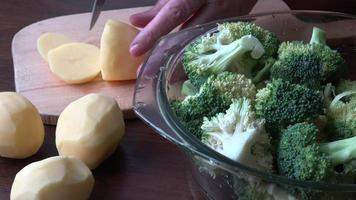 kvinna händer skärande potatisar i de kök. grön färsk broccoli. matlagning vegan mat. video