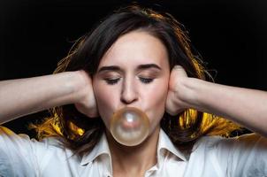 una hermosa chica de cabello oscuro infla una burbuja de chicle amarillo sobre un fondo negro foto