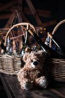 Teddy bear, champagne bottle with Christmas basket, gold garlands on dark brown wooden background, new year celebration concept photo