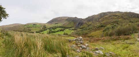 Panorama picture of typical Irish landscape with green meadows and rough mountains during daytime photo