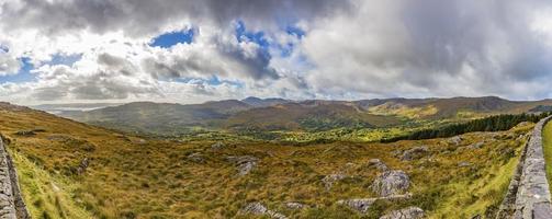 Panorama picture of typical Irish landscape with green meadows and rough mountains during daytime photo