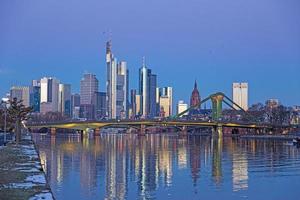 Picture of Frankfurt skyline during sunrise with reflections of skyscraper facades in Main river under cloudless and colorful sky photo