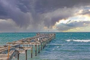 imagen de un embarcadero en ruinas con gaviotas descansando sobre él contra un cielo con nubes de tormenta foto