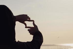 Planning and vision concept of new year's start, woman hands making frame gesture find focus at sunset, woman looking for perspective to capture the meaning of a clear upcoming target. photo