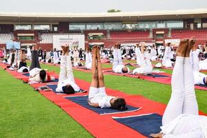 nueva delhi, india, 21 de junio de 2022 - sesión grupal de ejercicios de yoga para personas en el complejo deportivo yamuna en delhi el día internacional del yoga, gran grupo de adultos que asisten a clases de yoga en el estadio de cricket foto