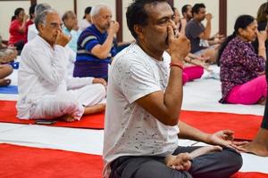 New Delhi, India, June 19 2022 -Group Yoga exercise session for people of different age groups in Balaji Temple, Vivek Vihar, International Yoga Day, Big group of adults attending yoga class in temple photo