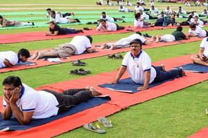 nueva delhi, india, 21 de junio de 2022 - sesión grupal de ejercicios de yoga para personas en el complejo deportivo yamuna en delhi el día internacional del yoga, gran grupo de adultos que asisten a clases de yoga en el estadio de cricket foto