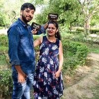 Indian couple posing for maternity baby shoot. The couple is posing in a lawn with green grass and the woman is falunting her baby bump in Lodhi Garden in New Delhi, India photo