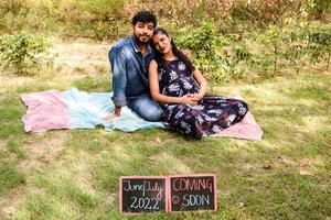 Indian couple posing for maternity baby shoot. The couple is posing in a lawn with green grass and the woman is falunting her baby bump in Lodhi Garden in New Delhi, India photo