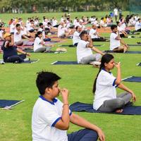 nueva delhi, india, 21 de junio de 2022 - sesión grupal de ejercicios de yoga para personas en el complejo deportivo yamuna en delhi el día internacional del yoga, gran grupo de adultos que asisten a clases de yoga en el estadio de cricket foto