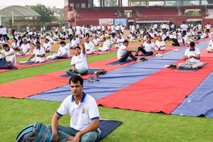 New Delhi, India, June 21 2022 - Group Yoga exercise session for people at Yamuna Sports Complex in Delhi on International Yoga Day, Big group of adults attending yoga class in cricket stadium photo