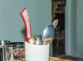 White container full of spoons, forks and knives on a table in a kitchen with a blurred background photo