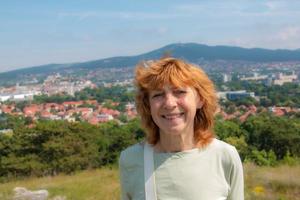 Portrait of a pretty aged woman against the backdrop of a typical European town with red roofs. Beautiful landscape with a blurred background. photo