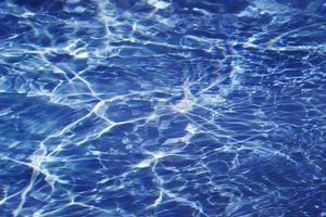 desenfoque borroso transparente color azul claro agua tranquila textura superficial con salpicaduras y burbujas. fondo de naturaleza abstracta de moda. ondas de agua a la luz del sol con cáusticos. agua azul brillando foto