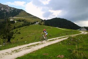 viaje a sankt-wolfgang, austria. un ciclista en el camino entre los campos con vista a las montañas y las casas en las nubes. foto