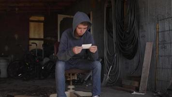 menino adolescente sorridente, jovem, sentado na garagem olhando a foto de família video