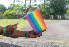 Asian or Thai gay hands wearing lgbtq wristband and holding rainblow flag as sign to protect and support gender diversity on pride month in lgbtq community photo